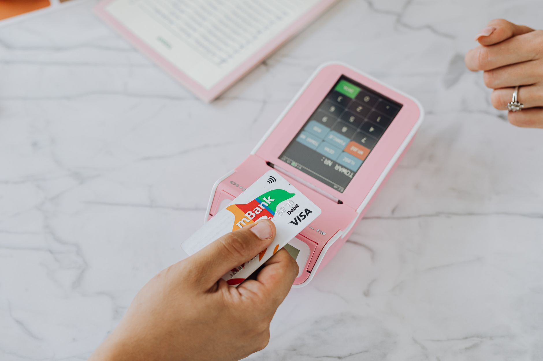 POS机一年要花多少钱:Hand using a contactless card on a pink POS term POS机一年要花多少钱:Hand using a contactless card on a pink POS term